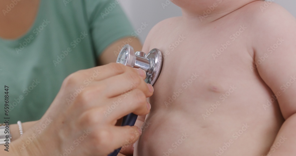 Handsome child sits at doctor checkup and puts pacifier in mouth. Pediatrician uses stethoscope to listen heartbeat and lungs of little kid. Mother with cute baby in hospital. Close up. Slow motion. Handsome child sits at doctor checkup and puts pacifier in mouth. Pediatrician uses stethoscope to listen heartbeat and lungs of little kid. Mother with cute baby in hospital. Close up. Slow motion.