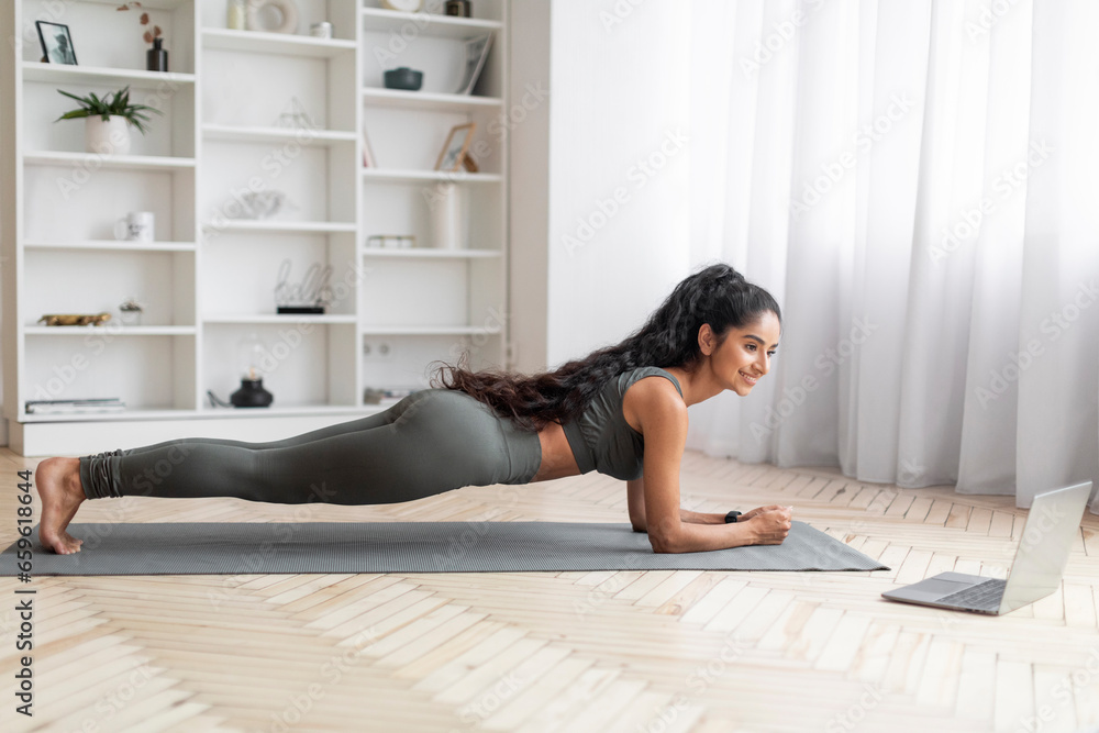 Maintaining Fitness: Young Lady Exercises via Laptop at Home Maintaining Fitness: Young Lady Exercises via Laptop at Home