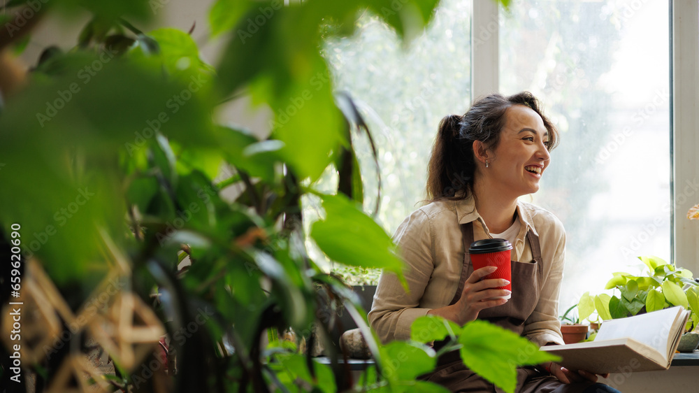 Cheerful asian floral business owner holding coffee to go and book near plants in flower shop Cheerful asian floral business owner holding coffee to go and book near plants in flower shop