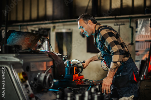 A tattooed metal turner operating a lathe machine, holding knobs.