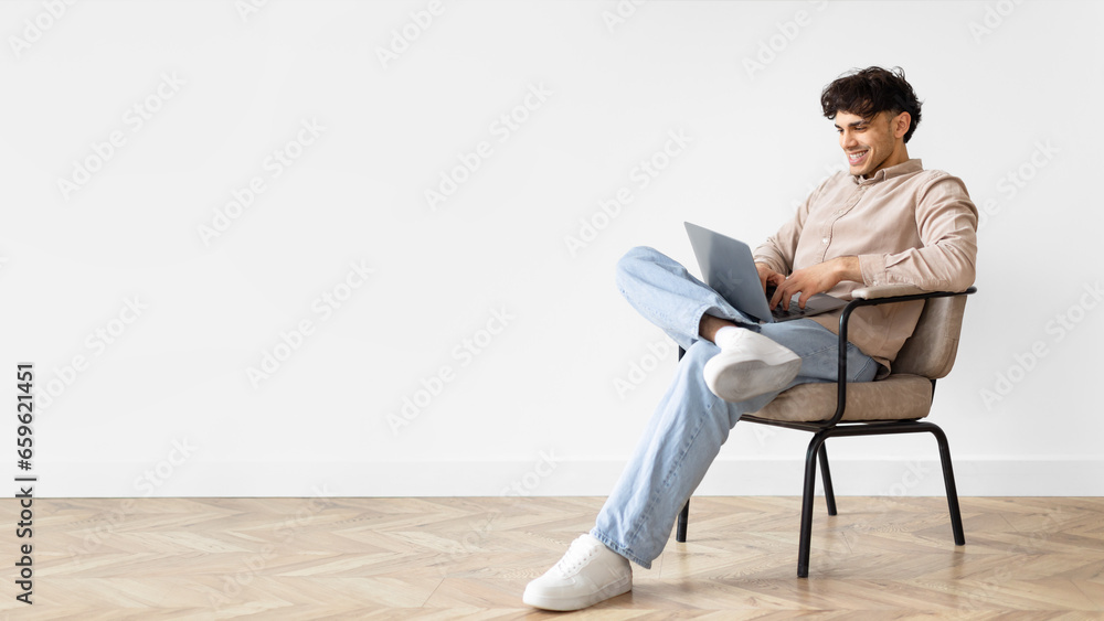 Freelancer Arabic Guy Websurfing On Laptop Sitting In Chair Indoor Freelancer Arabic Guy Websurfing On Laptop Sitting In Chair Indoor