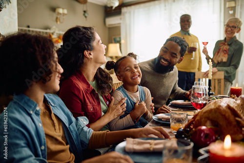 Happy multiracial extended family has fun and laughs while gathering for Thanksgiving in dining room.