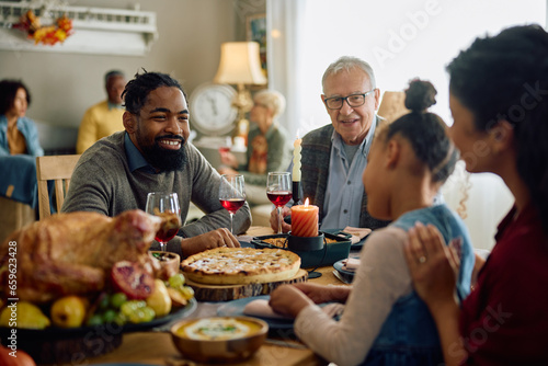 Happy black man talks to his family during Thanksgiving dinner in dining room.
