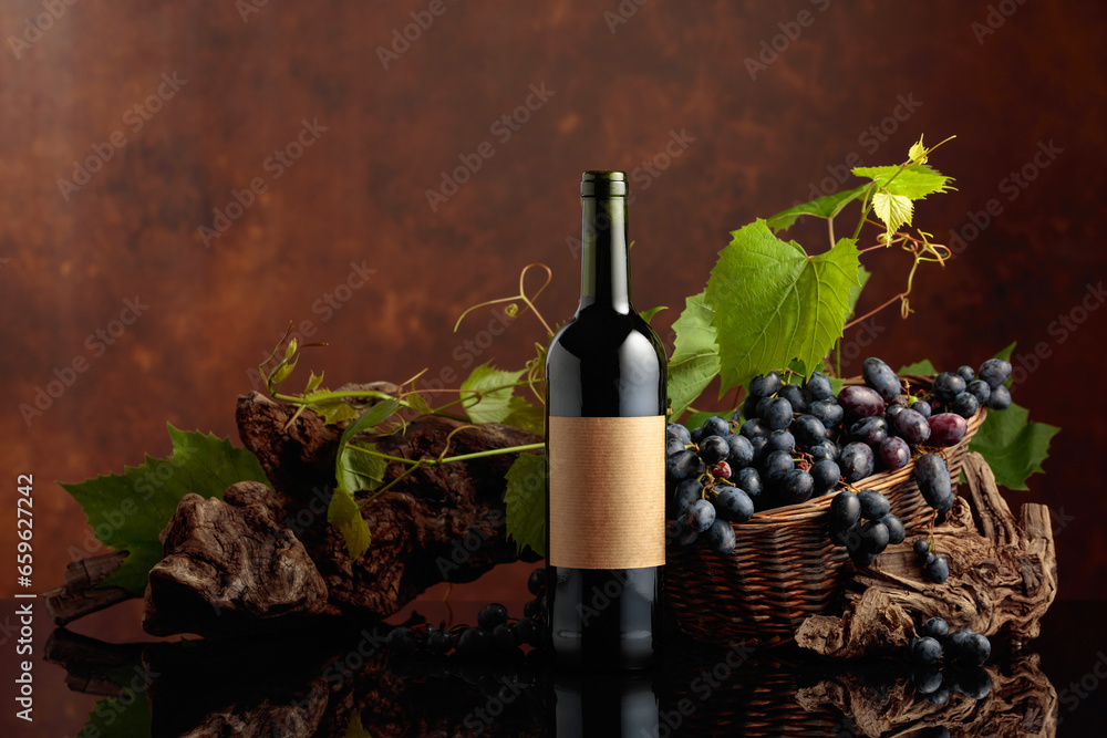 Bottle of red wine with blue grapes and vine branches.