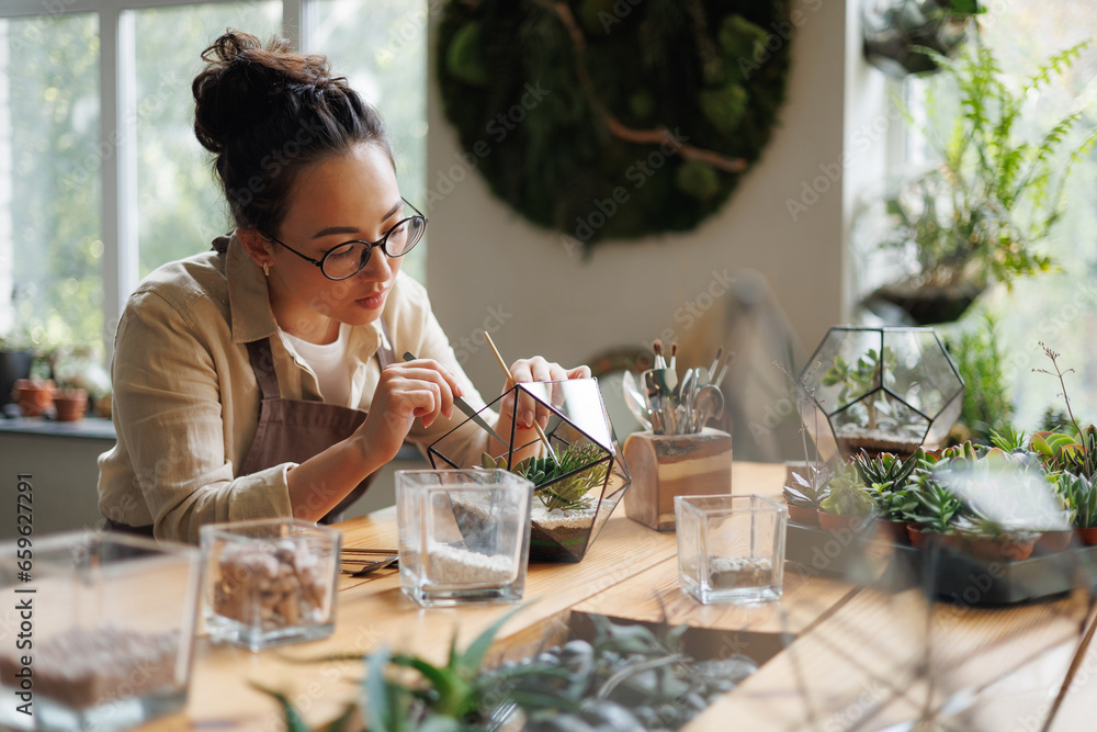 Asian florist making small garden with succulents in terrarium in floral shop Asian florist making small garden with succulents in terrarium in floral shop