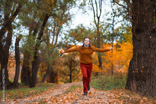 a young teenage girl runs through the autumn forest along a dirt road and enjoys the beautiful nature and bright yellow leaves