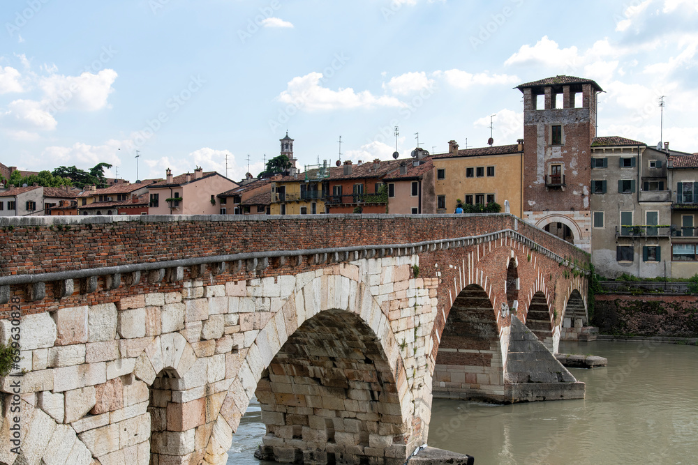 Side view of Ponte Pietra bridge over the Adige River in Verona, Italy with ancient houses along embankment the river