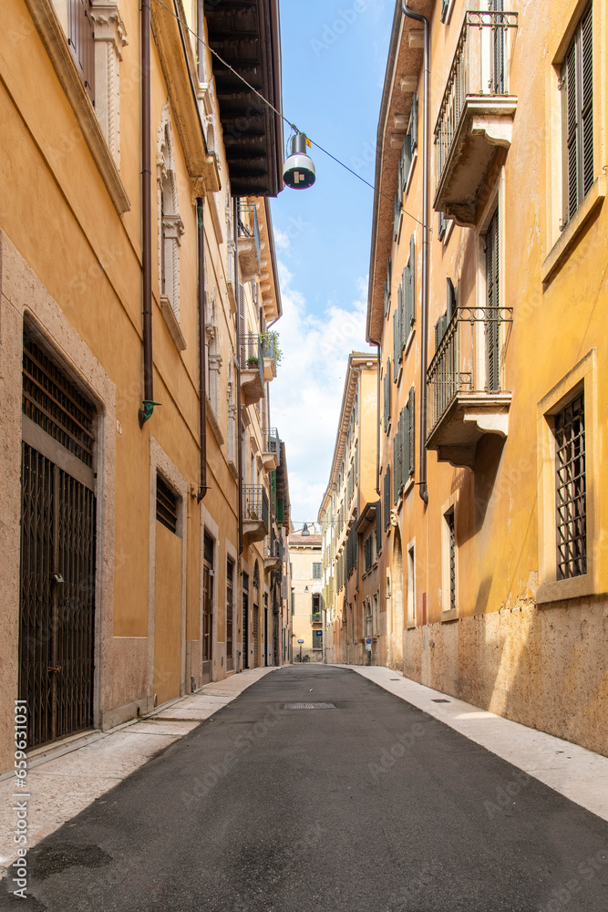 Low angle view down a typical historic narrow street in an Italian city with yellow plastered walls and high enough to provide shade in warm sunny summers