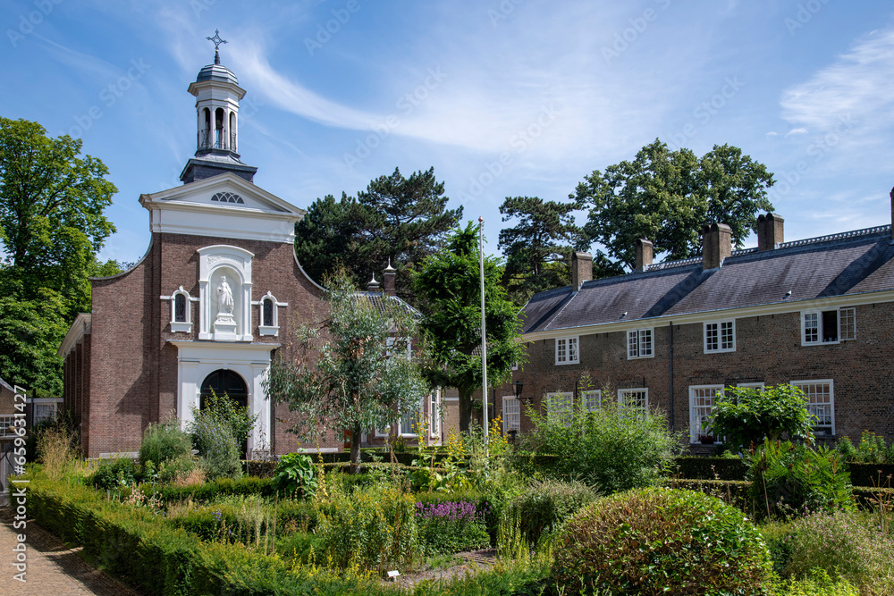 Courtyard of the beguinage (Begijnhof) in Breda, the Netherlands with herb garden and surrounded by 29 small houses and Catharina churck in background