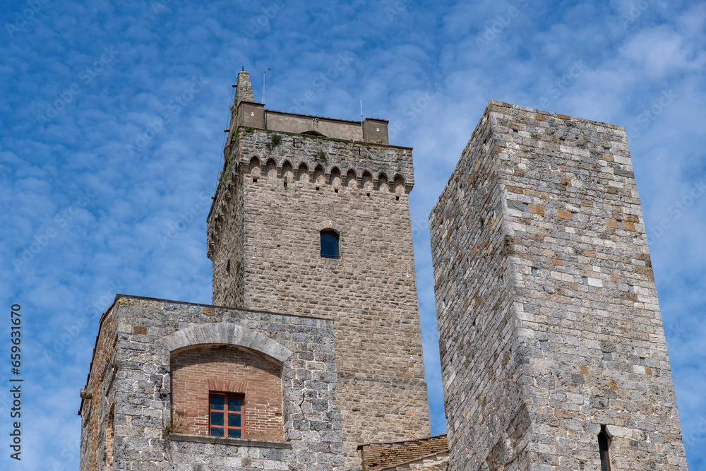Low angle view of some of the towers in San Gimignano, Italy, a  small walled medieval hill town in the province of Siena, Tuscany against a white clouded blue sky