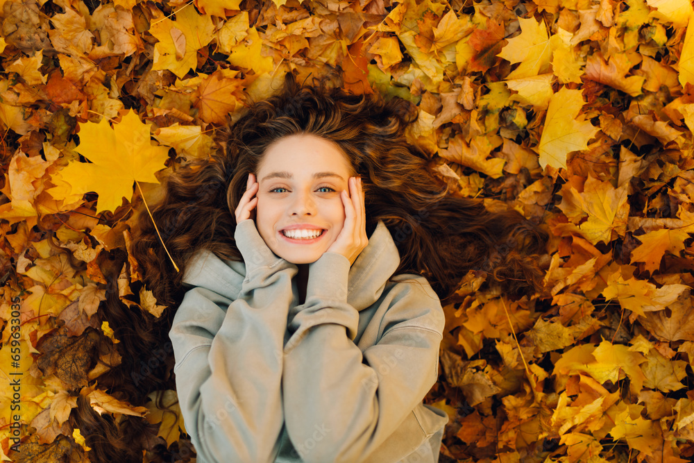 Smiling young woman lies on the autumn foliage in the forest with the yellow leaves Smiling young woman lies on the autumn foliage in the forest with the yellow leaves