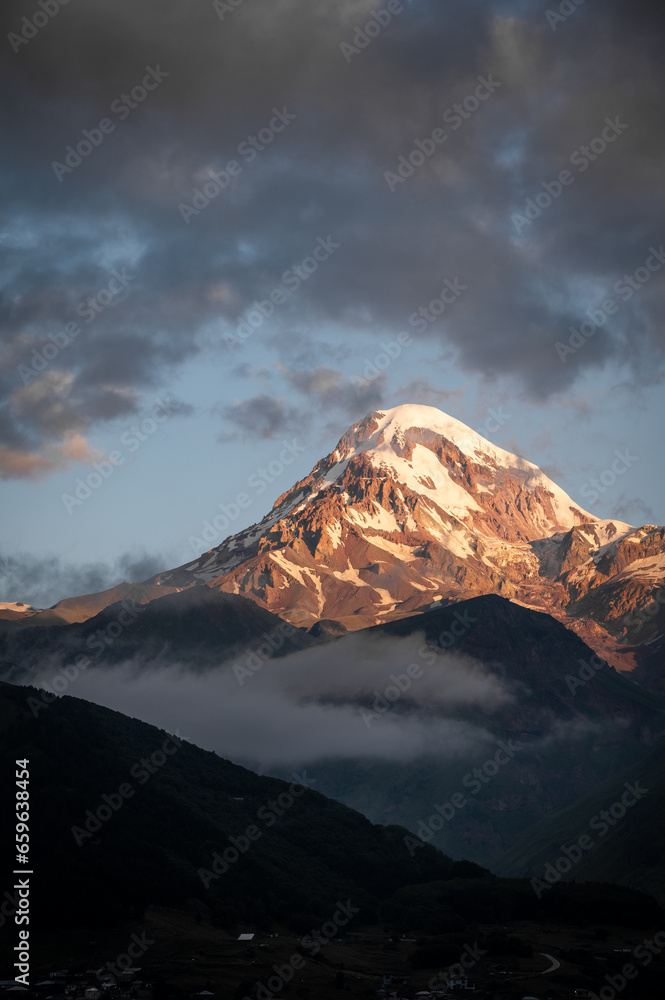 An Early morning view of a snowcapped Kazbegi Mountain with clouds surrounding it