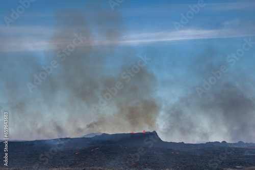 Close up view of spatter cone of fissure near Litli-Hrútur Hill during the 2023 eruption near the mountain Fagradalsfjall, Iceland volcano area with dark smoke clouds of wildfires above landscape