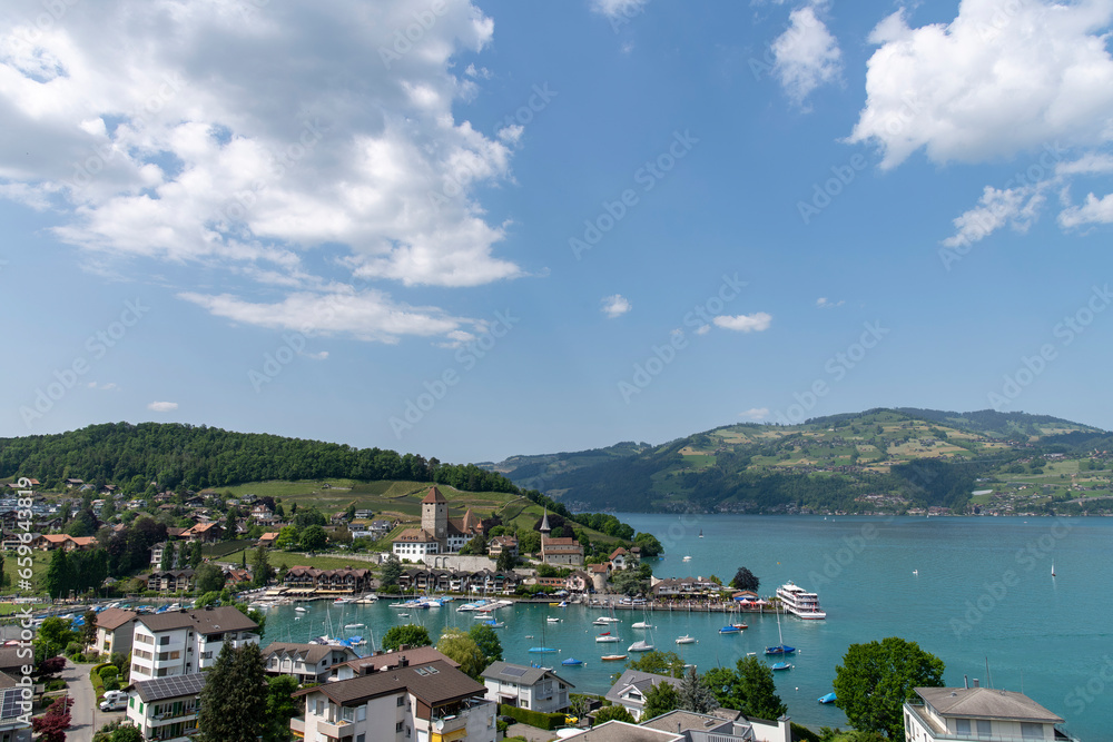 Panoramic view over the city of Spiez, Switzerland with its medieval Spiez Castle along the Thunersee against a white clouded blue sky