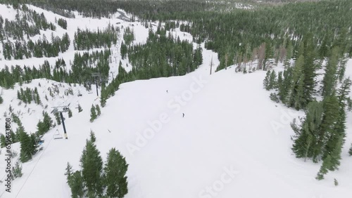 Aerial view of snowboarder in Mammoth Lakes resort in Sierra Nevada, California. Ski resort piste with people snowboarding in evergreen spruce forest with green pines trees. Ski area mountain resort