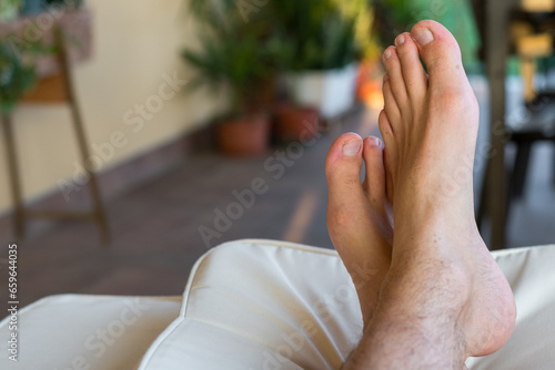 Male feet in the foreground crossed and resting on cushions on the terrace. Relaxing day and view of some green plants in the background. Perfect for copy space. photo