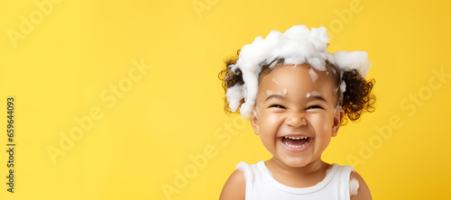 banner copyspace Little smiling african American baby girl with ponytails big soap foam on head in hair. on solid yellow background, Shampoo, hair treatment and soap for children, childs bathing time