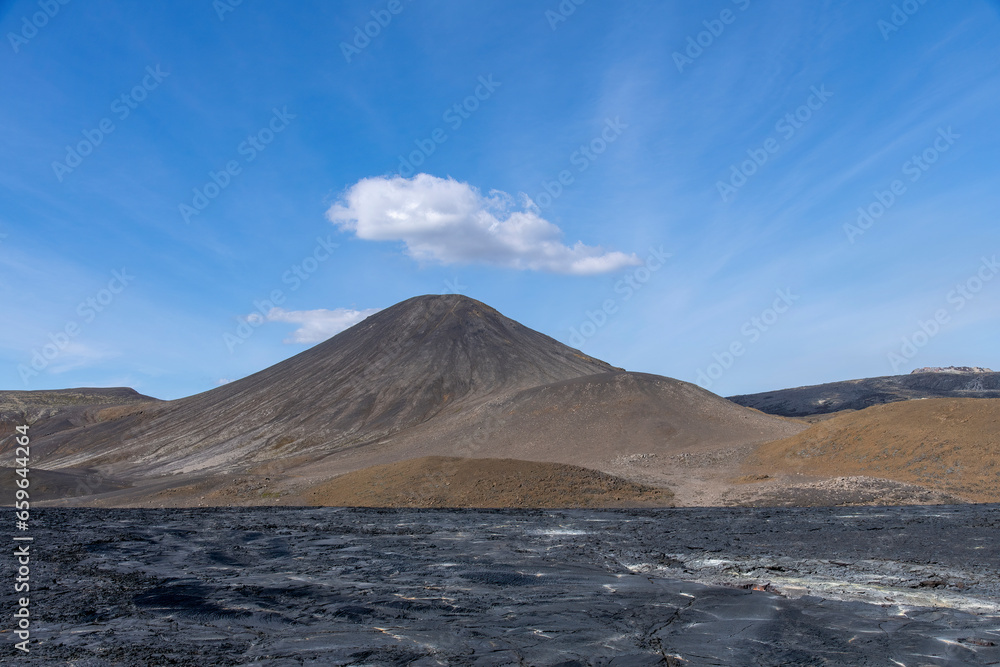 Panoramic view over volcanic landscape on Reykjanes Peninsula, Iceland, near mountain Fagradalsfjall volcano area with black lava field in foreground against a white clouded blue sky