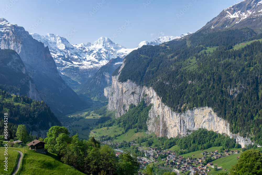 Panoramic view over Lauterbrunnen, Switzerland with high cliffs and Staubbach Waterfall and snowcapped mountains of Bernese Alps in background
