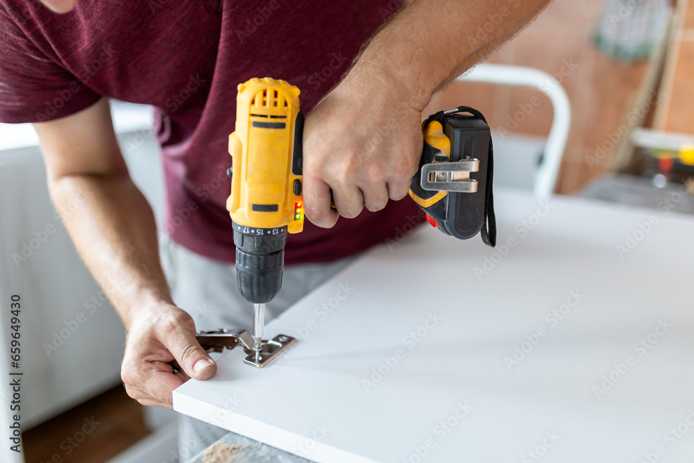 Man holding cordless screwdriver machine and screws lie for screwing a screw assembling furniture at home - obrazy, fototapety, plakaty 