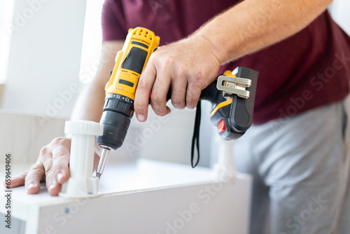 Furniture assembler man holding screwdriver for assembling kitchen wooden rack and attaching legs