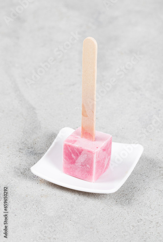 Cold dessert. Raspberry ice cream in the shape of small cube on a wooden stick. On a plate. Close u