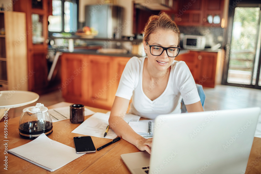 Happy young woman using her laptop in the kitchen at home Happy young woman using her laptop in the kitchen at home