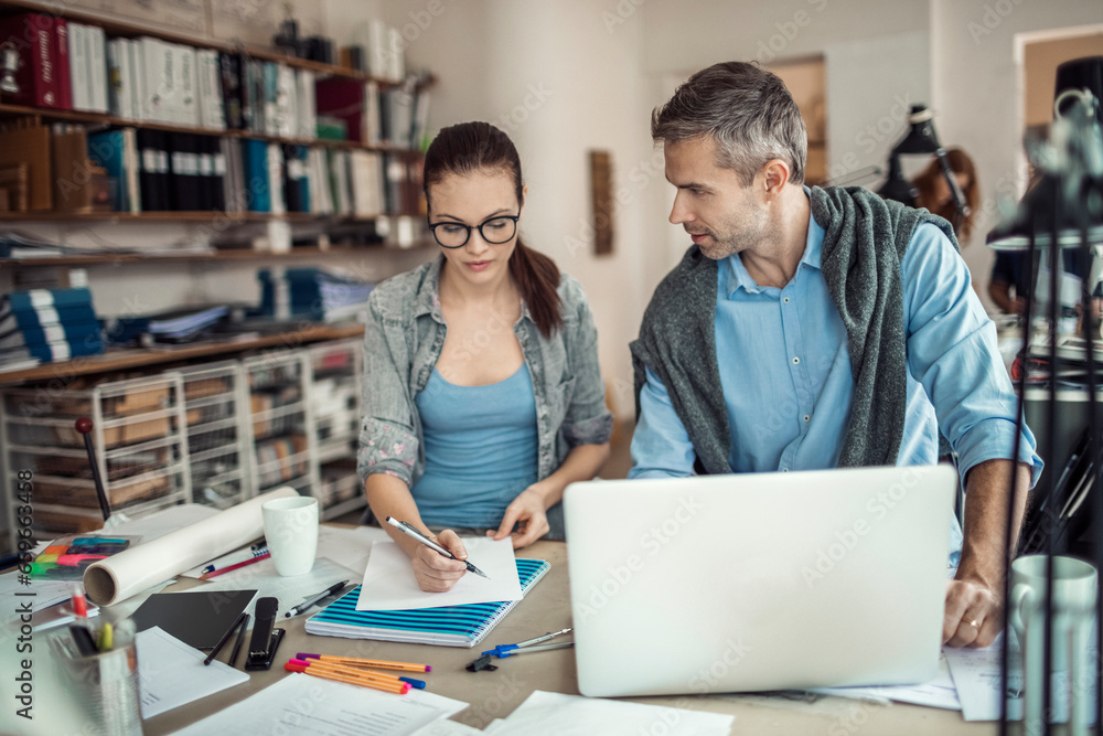 Young man and woman working together on a project in a startup company office Young man and woman working together on a project in a startup company office