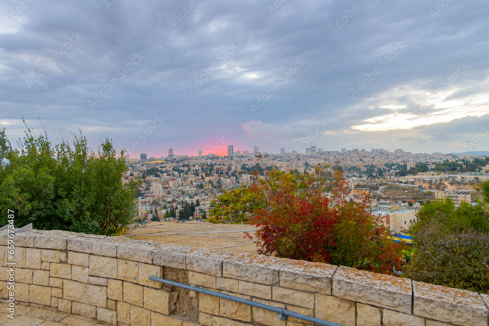 Hillside view of the city of Jerusalem, Israel, as the sun sets and glows red behind the cityscape.