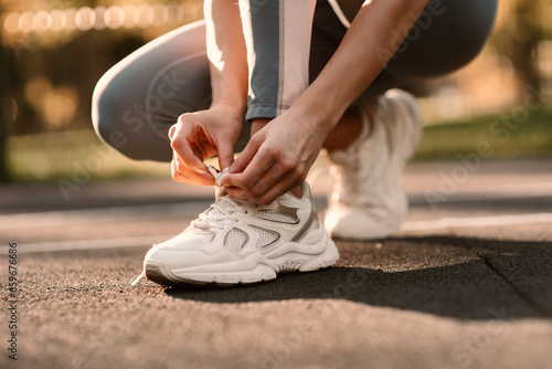 An athlete ties a white sneaker in a close-up on a sports field. Fintes in the open air.