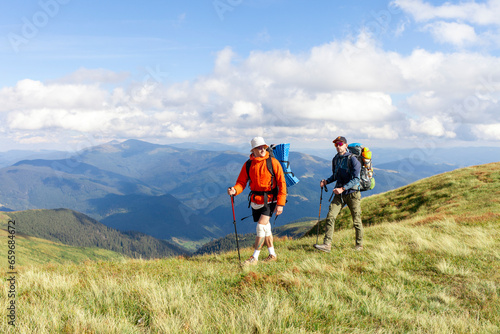 two men with hiking equipment and backpacks go to the mountains with trekking poles