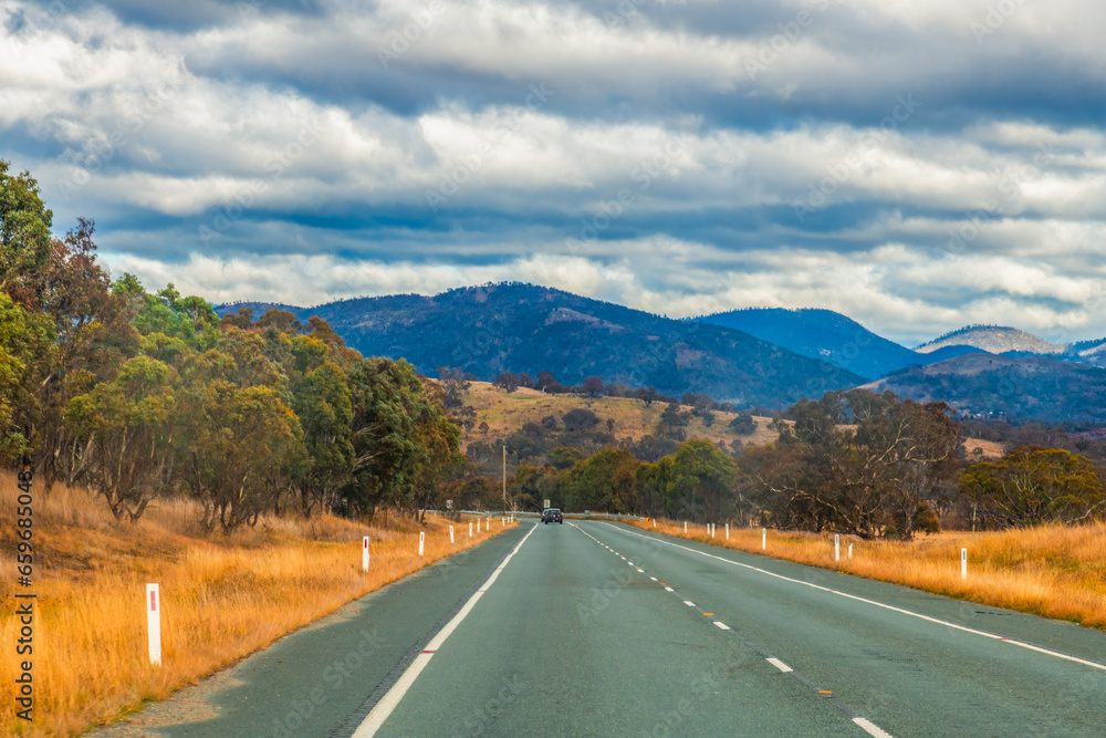 Fototapeta premium Road trippin through the dry countryside under a blue sky with clouds