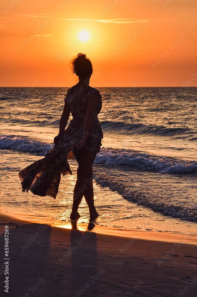 Woman on the seashore in a beautiful evening scenery. Girl walking on the beach with the setting sun in the background. Photo taken at the Baltic Sea in Leba, Poland.