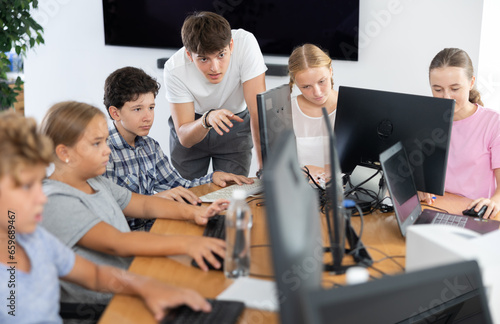 Young guy teacher teaches boy student to work with computer at lesson in classroom