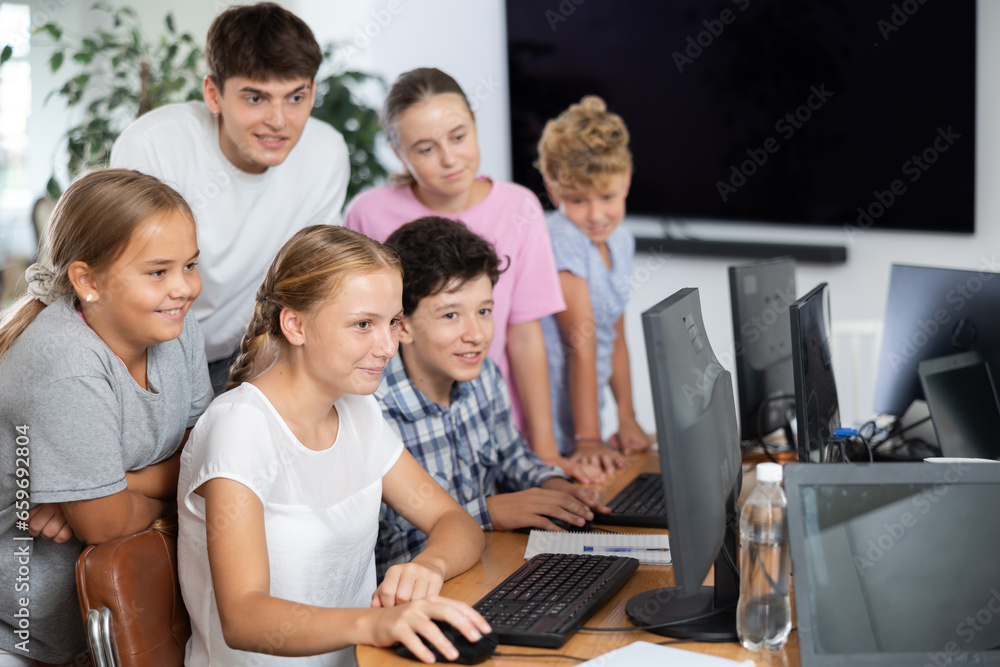 Interested preteen boys and girls working on computer together with teacher in IT cabinet