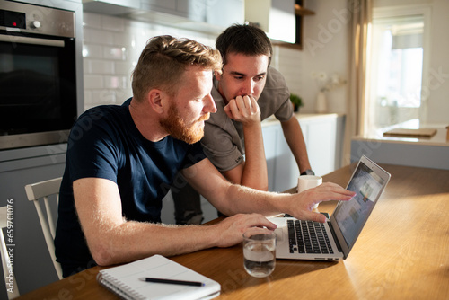 Young male gay couple browsing on the laptop together at home