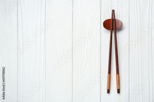 Pair of chopsticks with rest on white wooden table, top view. Space for text