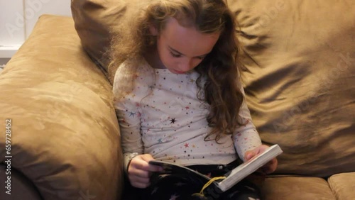 LITTLE GIRL READING A BOOK ALONE ON THE COUCH photo