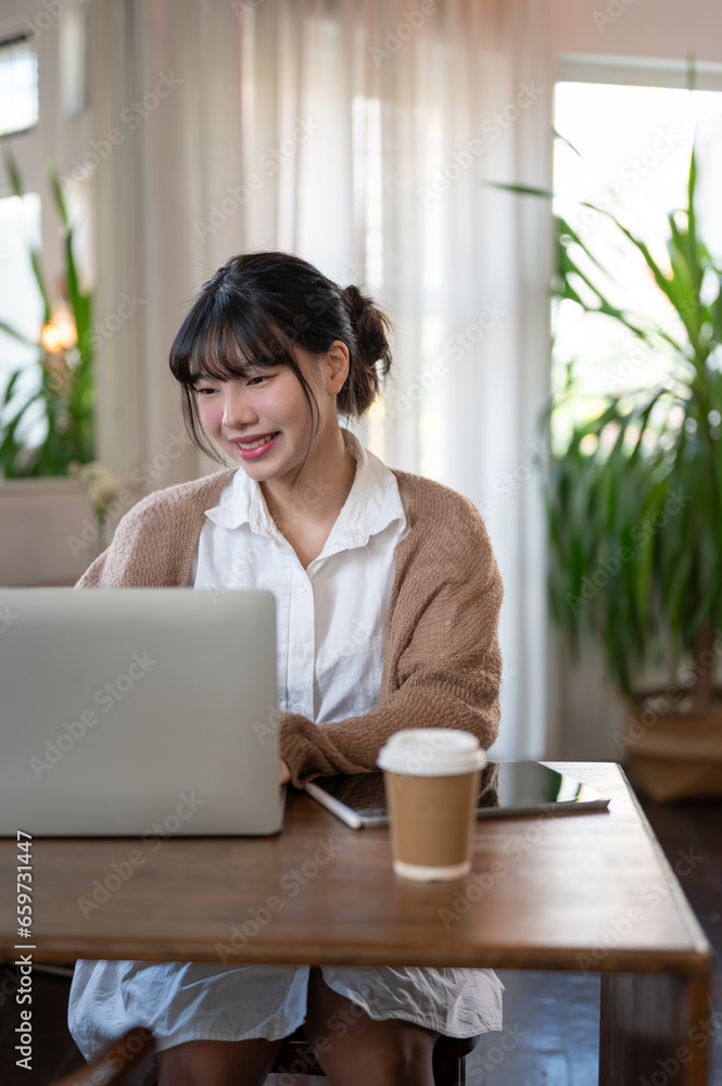A beautiful young Asian woman working remotely at a cosy coffee shop, working on her laptop. A beautiful young Asian woman working remotely at a cosy coffee shop, working on her laptop.
