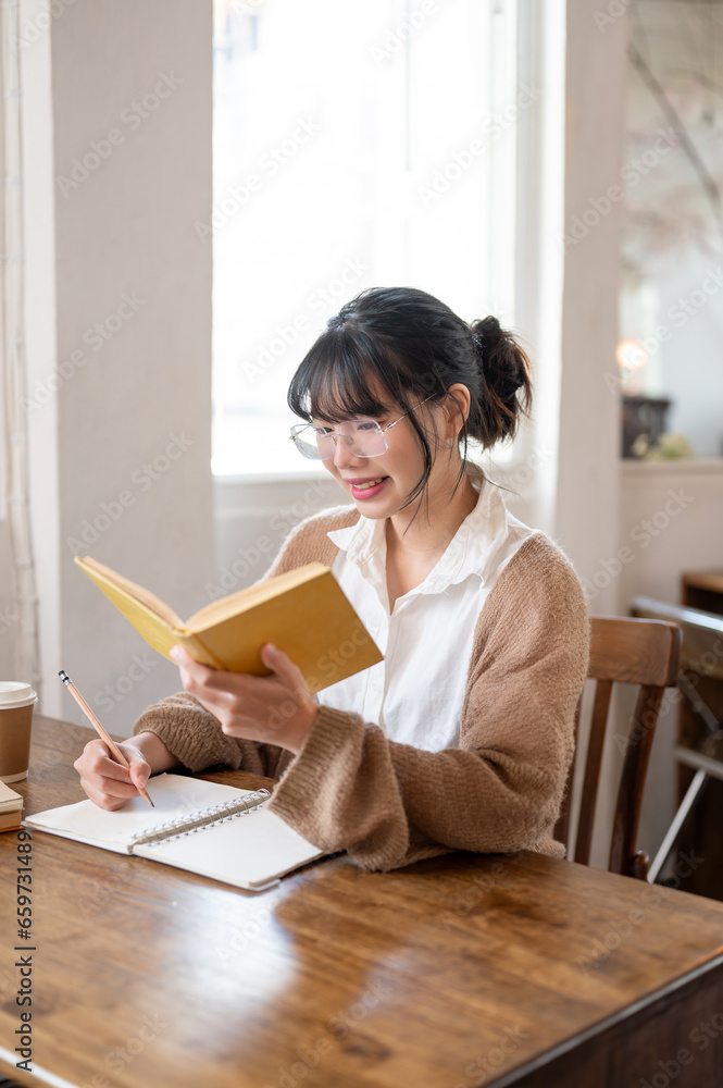 A focused Asian female student doing her homework, researching information in a book at a table. A focused Asian female student doing her homework, researching information in a book at a table.