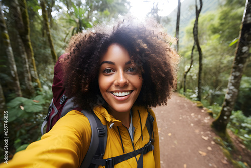 Happy traveller black woman with backpack taking selfie picture in forest- Travel blogger taking self portrait with smart mobile phone device outside - Life style and technology concept photo