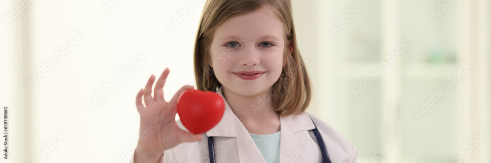 Positive little girl in uniform of doctor holds red heart Positive little girl in uniform of doctor holds red heart