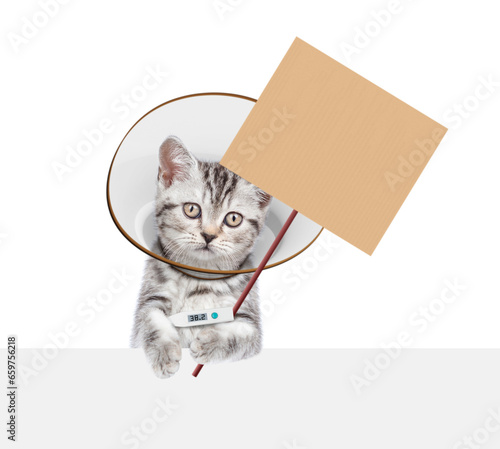 Fototapeta Naklejka Na Ścianę i Meble -  Cute tabby kitten wearing protective cone collar looking above empty white banner. Isolated on white background