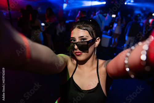 beautiful latin woman with sunglasses taking a selfie photo. In the background there are unrecognizable people. © PH German Alvarez