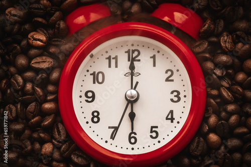 Red alarm clock on a background of coffee beans. A close-up of the alarm clock shows six o'clock in the morning. Coffee in the morning.