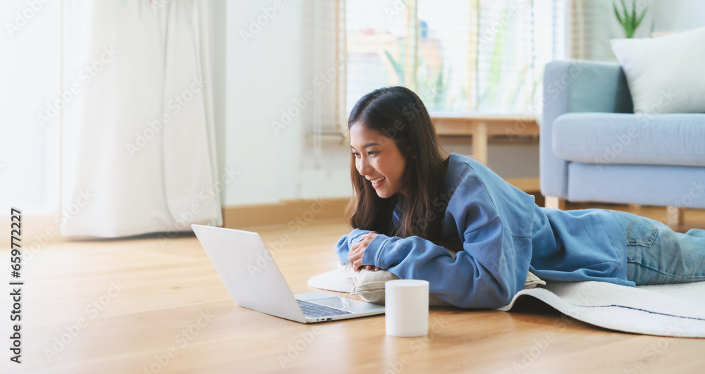 Young asian woman smile working in living room at home. Happy female using computer laptop and lying on the floor at house, Video call with friend Young asian woman smile working in living room at home. Happy female using computer laptop and lying on the floor at house, Video call with friend