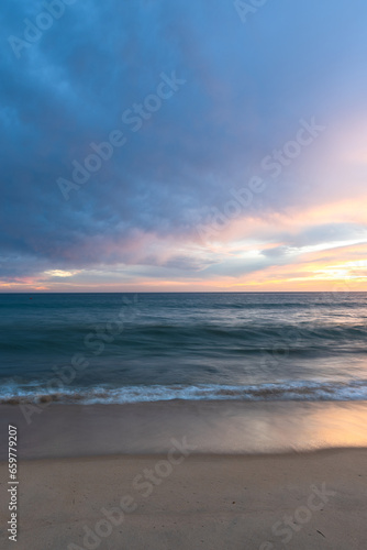 Sunset on sandy beach with ocean waves and colorful sky and clouds, Algarve, Portugal