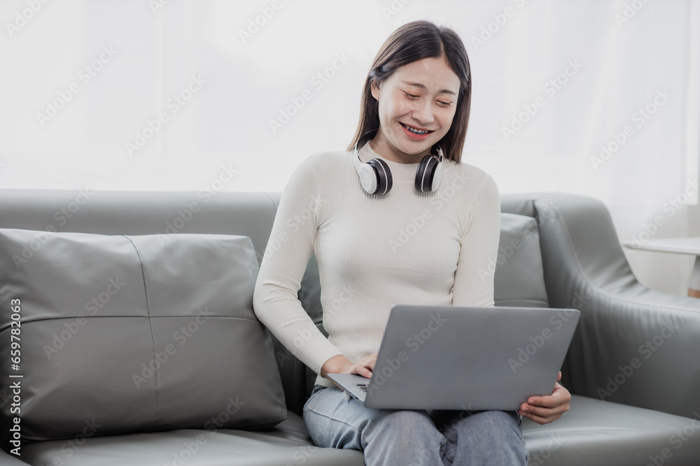 Asian woman surfing social media with headphones using laptop at home on sofa Asian woman surfing social media with headphones using laptop at home on sofa