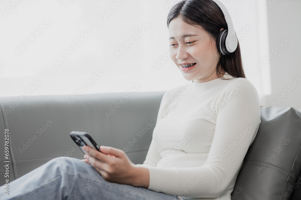 Asian woman surfing social media with headphones using laptop at home on sofa Asian woman surfing social media with headphones using laptop at home on sofa