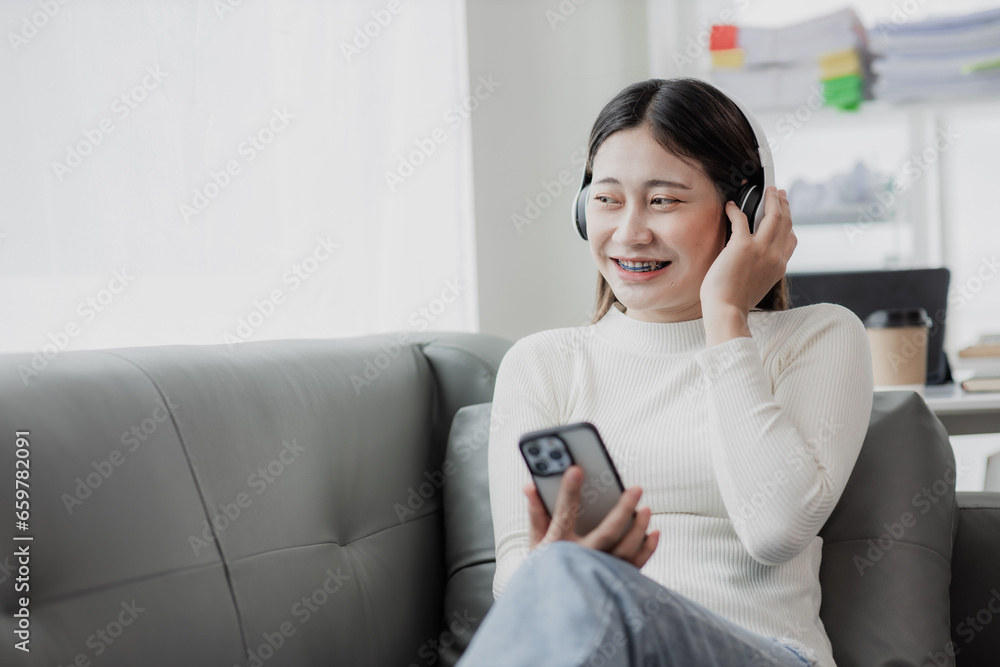 Asian woman surfing social media with headphones using laptop at home on sofa Asian woman surfing social media with headphones using laptop at home on sofa
